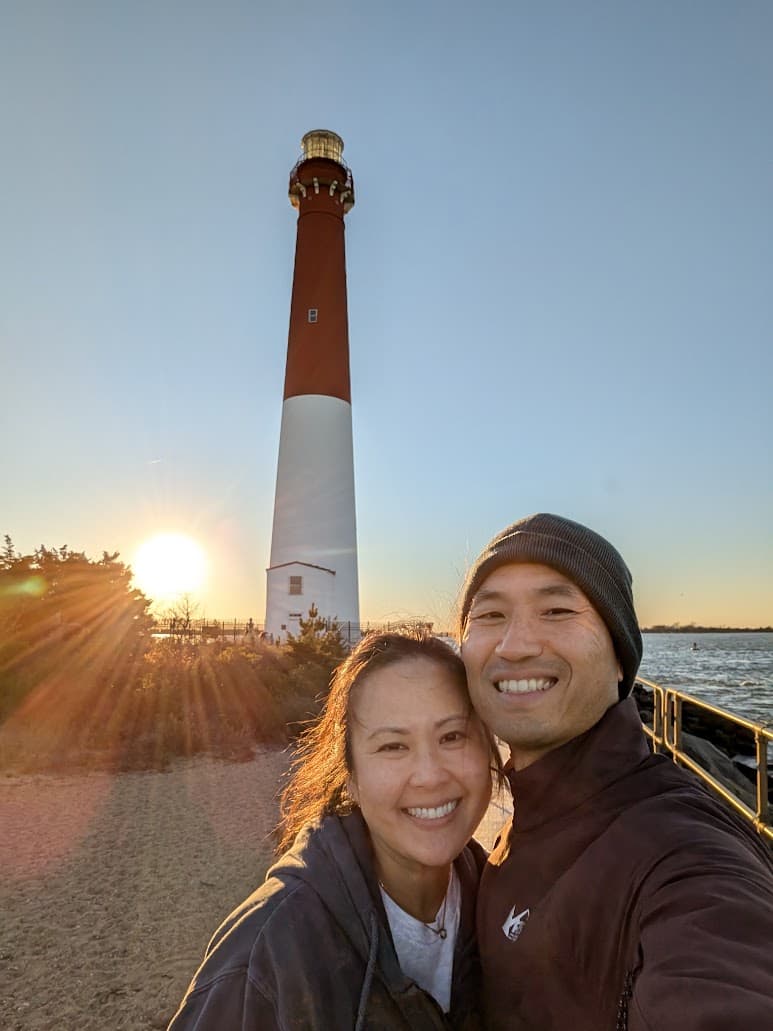 Janet and James smiling together at the beach with a lighthouse behind them.